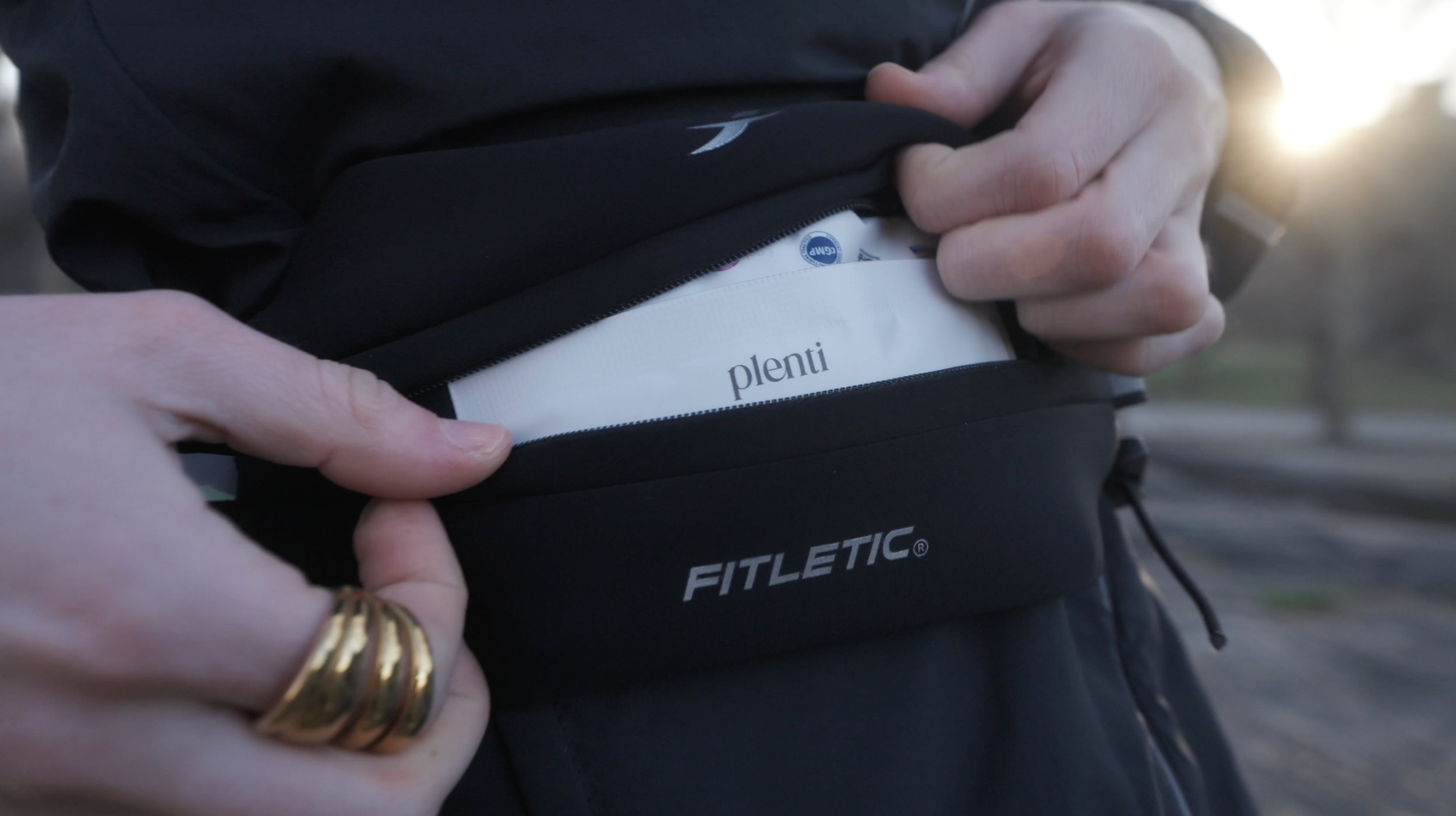 Person opening a black bag to reveal a white package labeled 'plenti' inside, with an outdoor setting in the background.