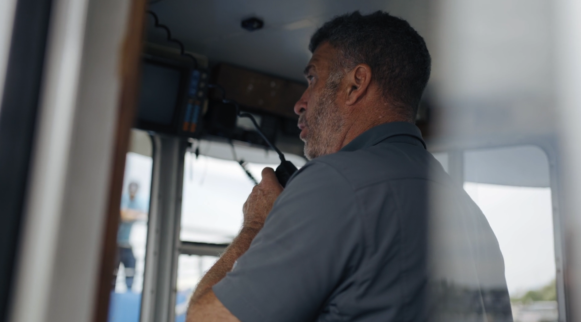 A man using a radio microphone inside a boat's control cabin.