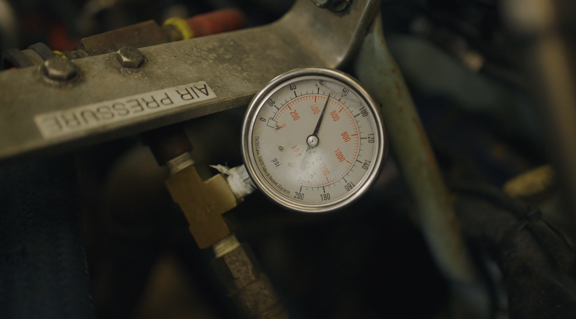 An automotive gauge displaying pressure in psi and kp on a rusty engine part with a label that reads 'AIR PRESSURE'.