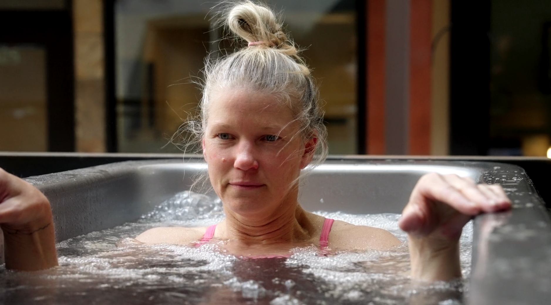 A woman with gray hair tied in a bun relaxing in a hot tub or Jacuzzi outdoors.