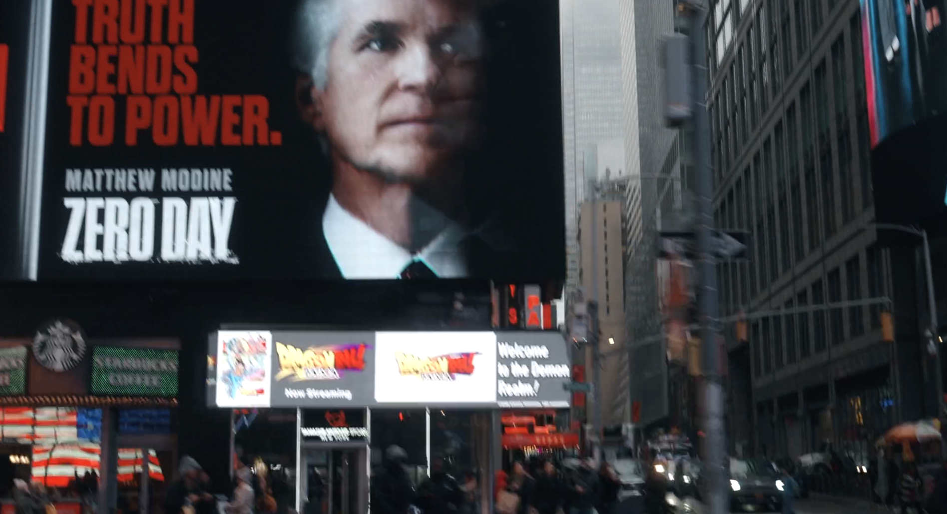 Billboard with a close-up of Matthew Modine's face and text about 'Zero Day' in Times Square, New York City. Smaller electronic signs below with advertisements and information.