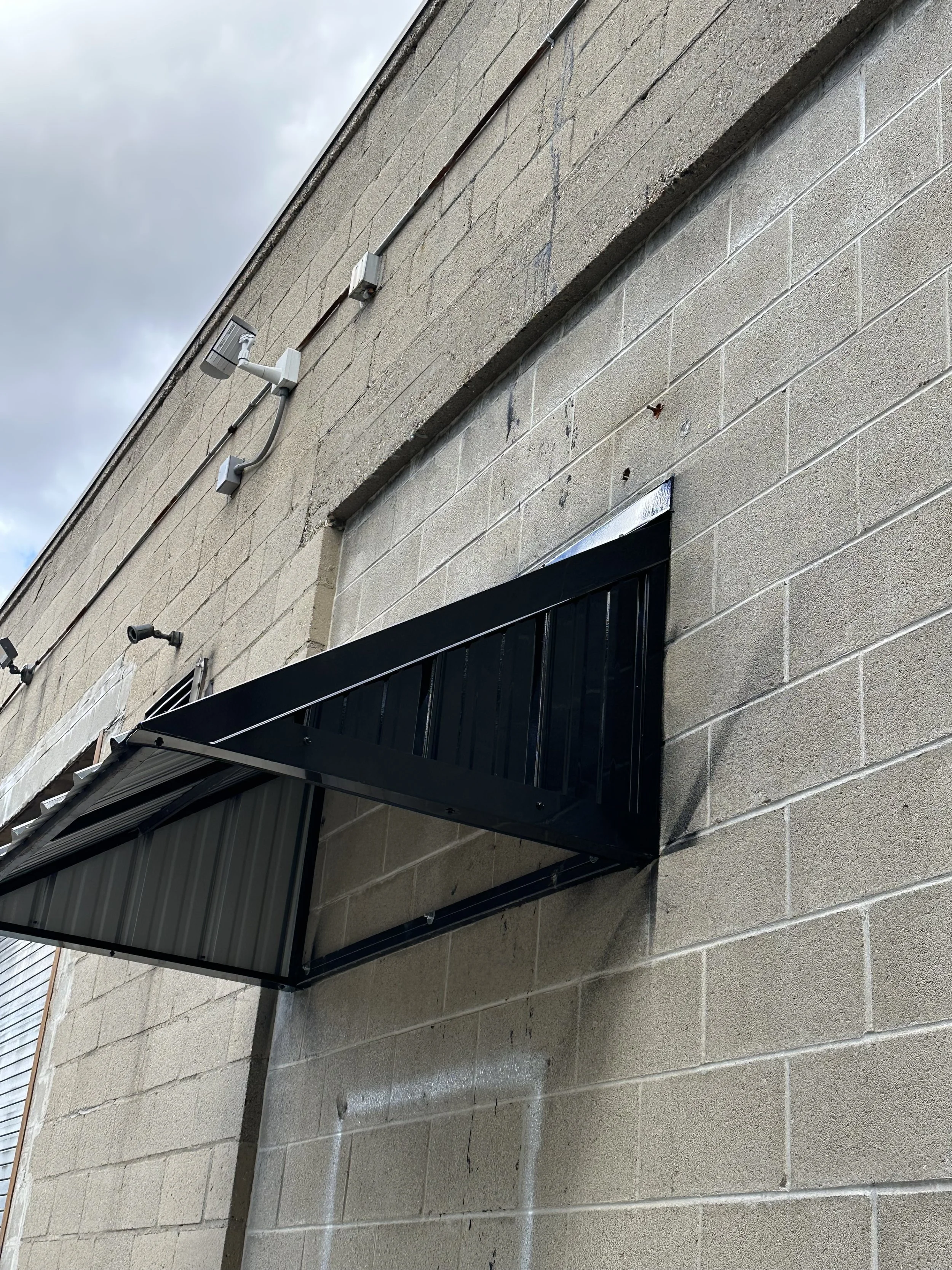 Close-up of a beige brick building wall with black metal awning and security cameras installed above.