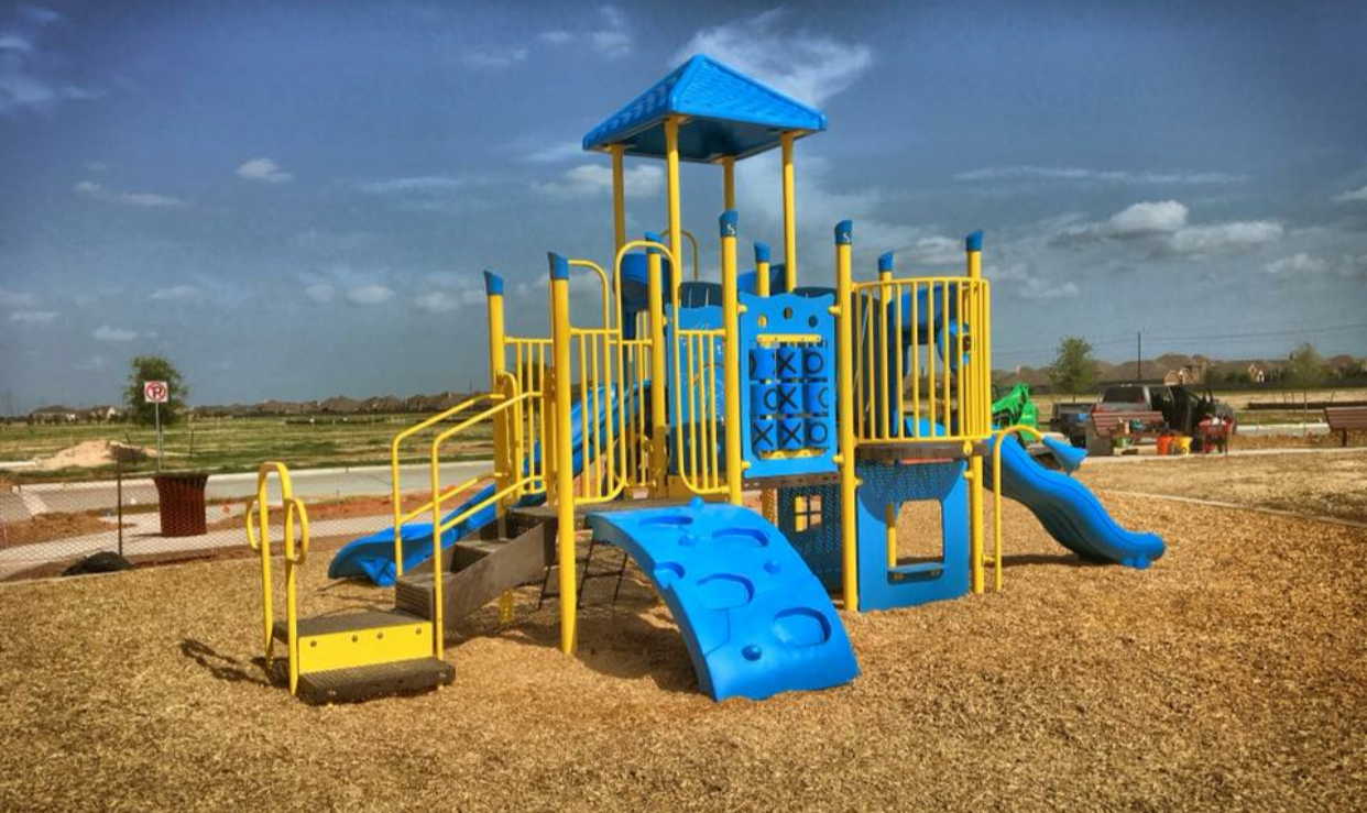 Colorful playground structure with blue and yellow equipment, slides, and climbing features, located in an outdoor park under a partly cloudy sky.