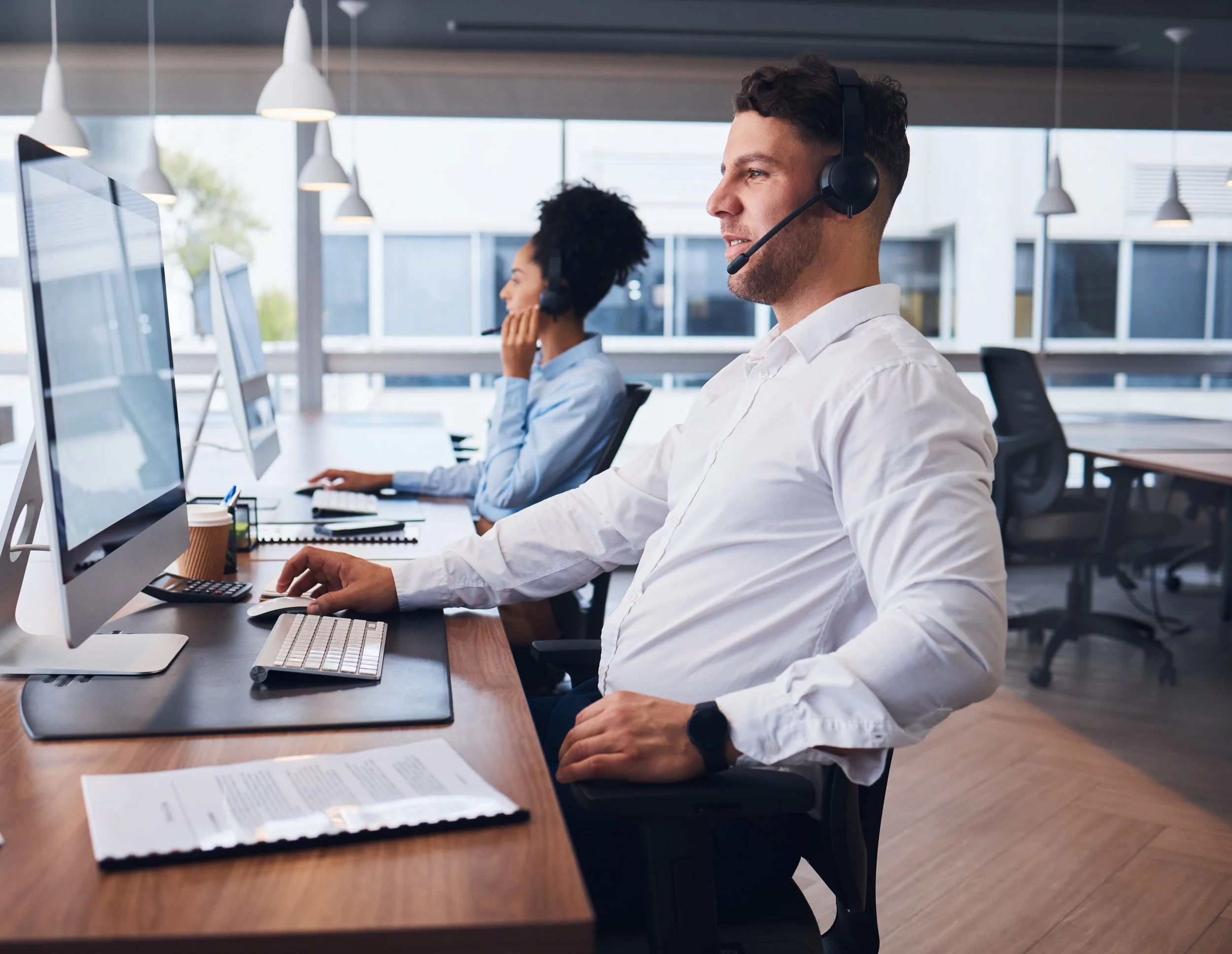 Two customer service representatives with headsets working at computers in an office.