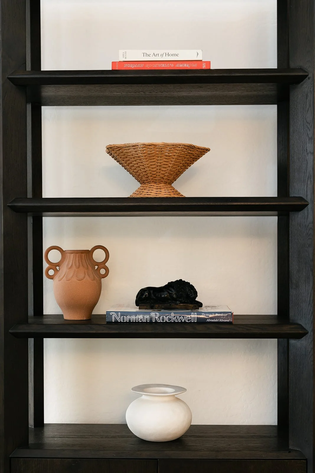 Black framed bookshelf with three shelves displaying various decorative objects and books, against a white wall.