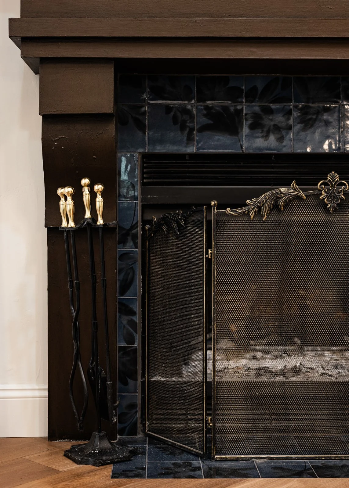 Black fireplace with a decorative metal screen and gold fireplace tools.