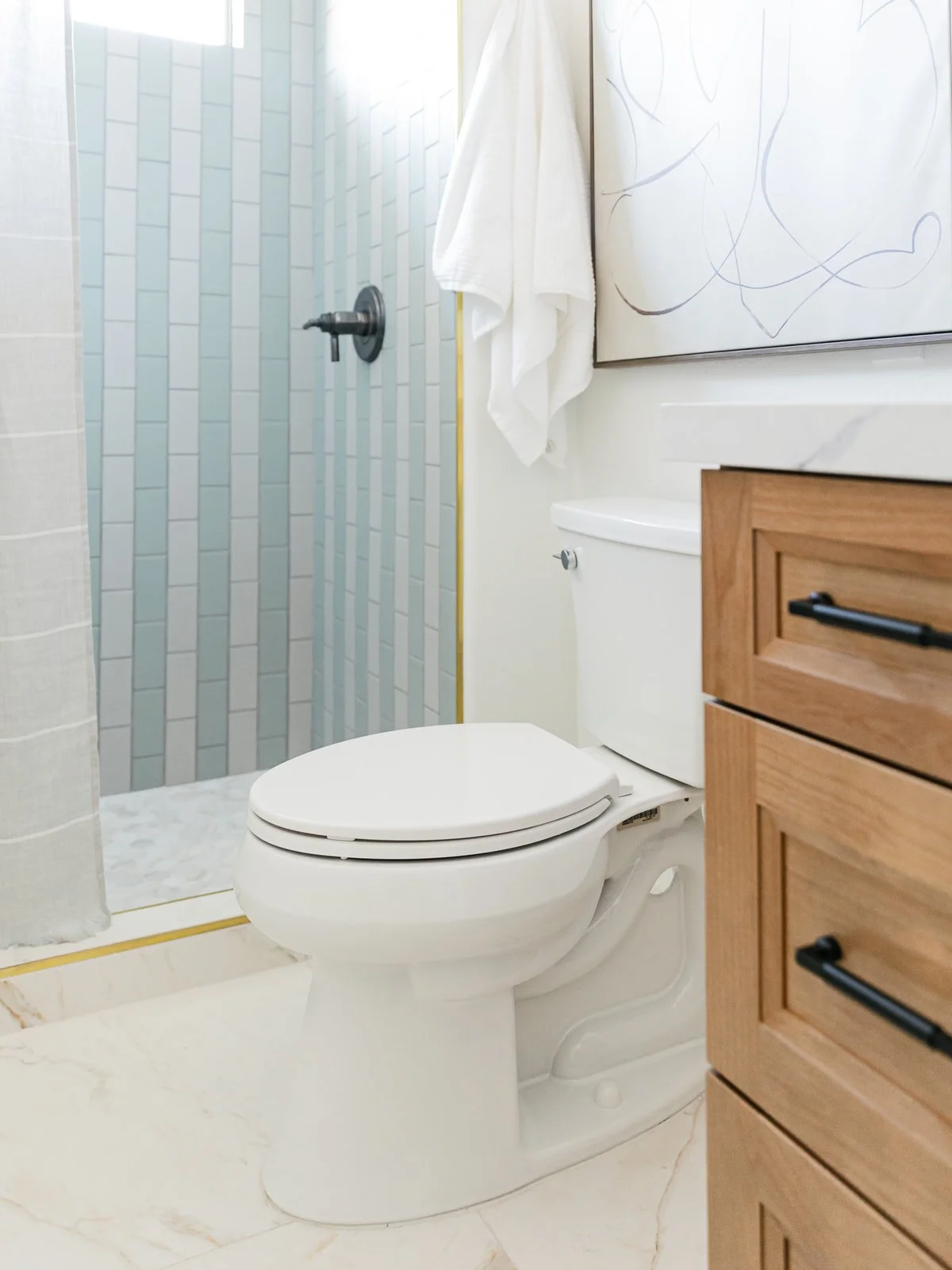 A bathroom with a white toilet, a wooden cabinet, and a shower area with light blue tiles and a curtain.
