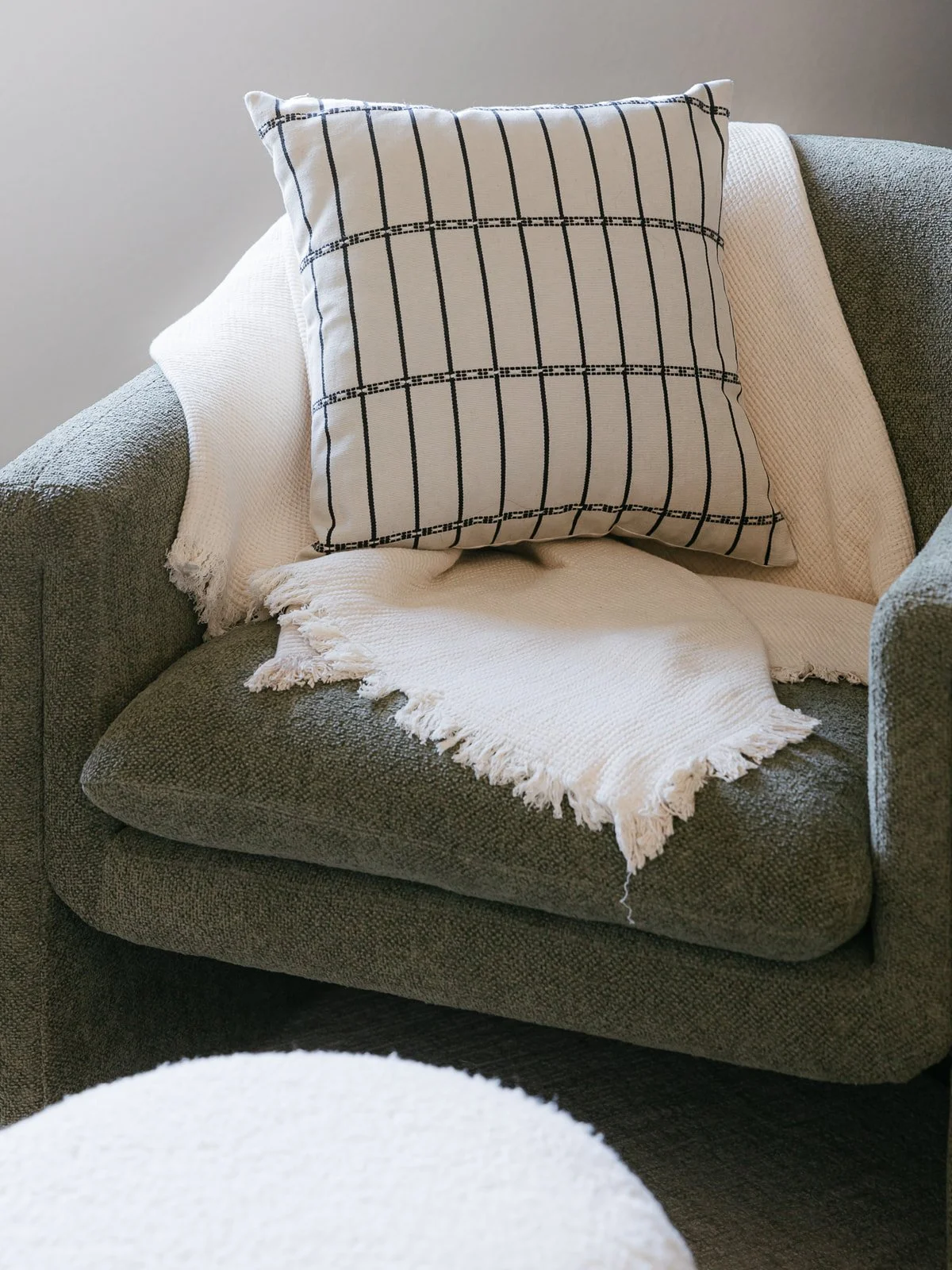 A gray upholstered armchair with a white woven throw blanket and a square pillow with a black and white checkered pattern.