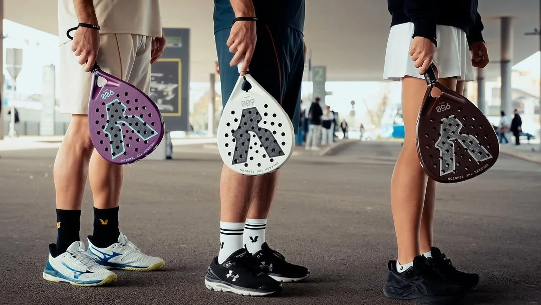 Três pessoas com roupas esportivas segurando discos de padel em um ambiente externo, possivelmente uma quadra ou área de lazer.
