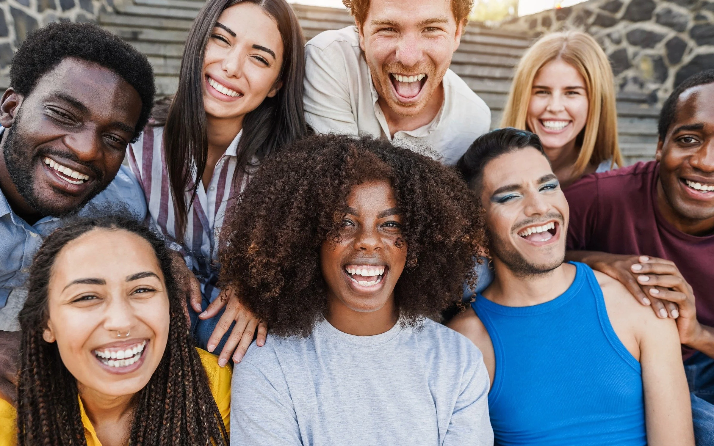A diverse group of young adults smiling and laughing together outdoors on steps.