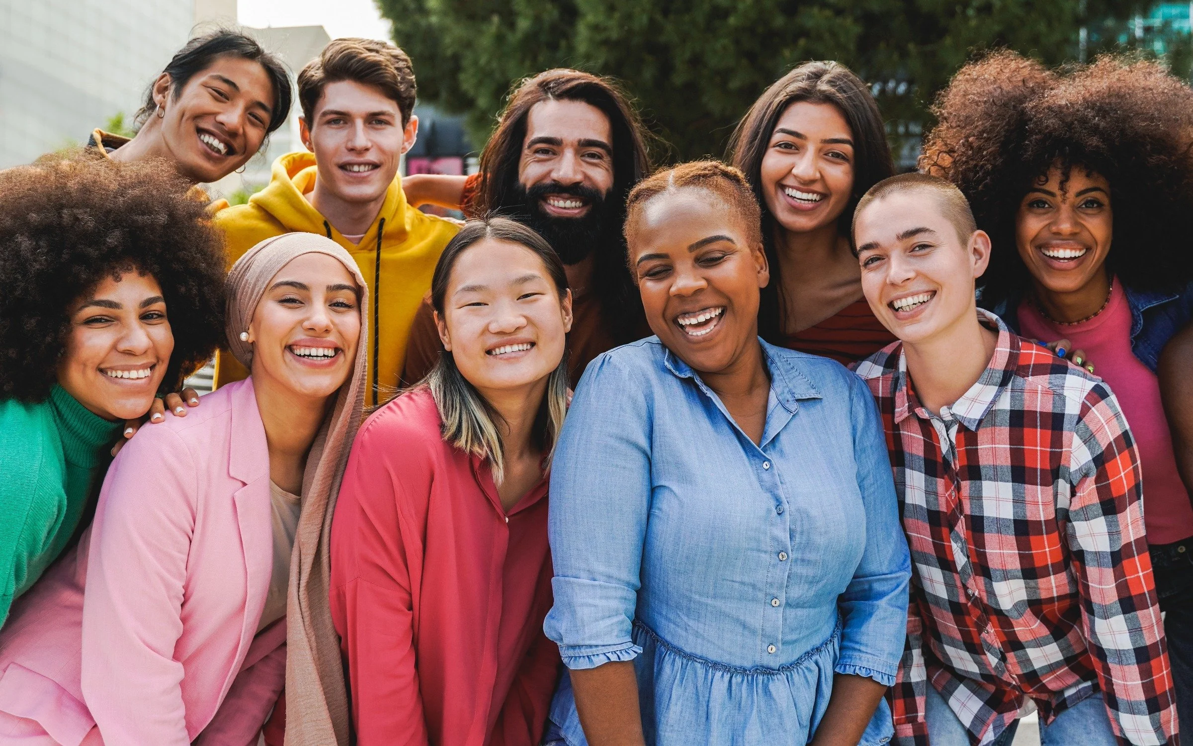 A diverse group of eleven people smiling and posing outdoors in a park.