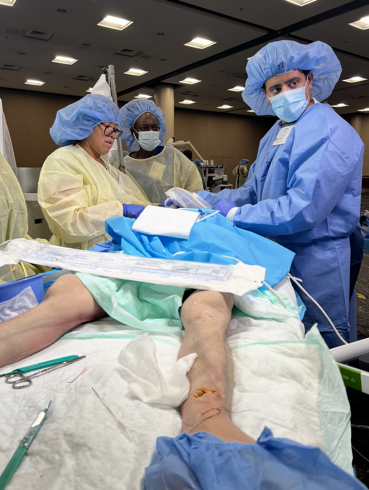 Medical team performing surgery on a patient's leg, with the patient's leg extended on a surgical table. The team is dressed in surgical gowns, masks, and caps.