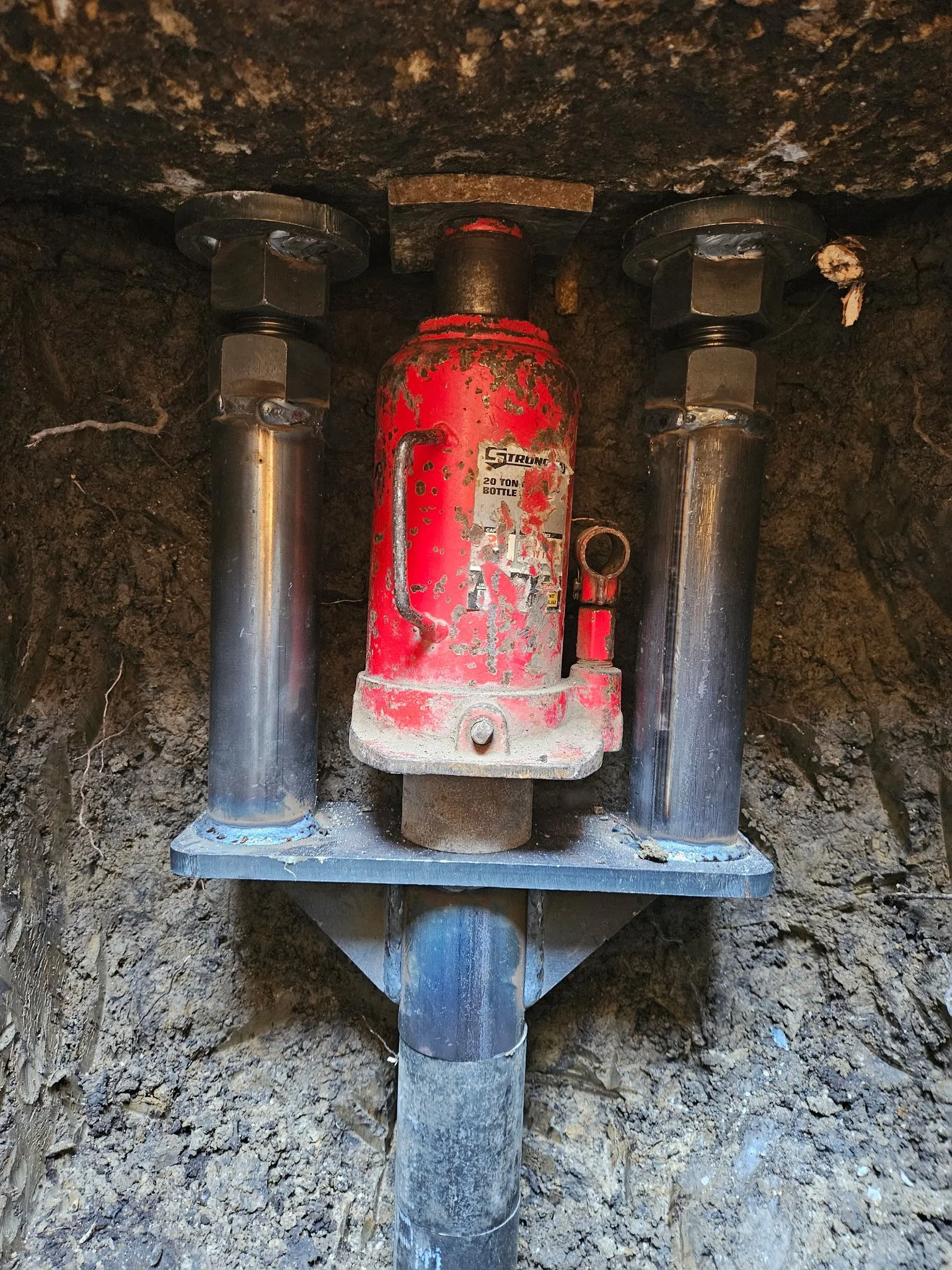 Underground utility vault with a red valve and two supporting pipes, surrounded by dirt.