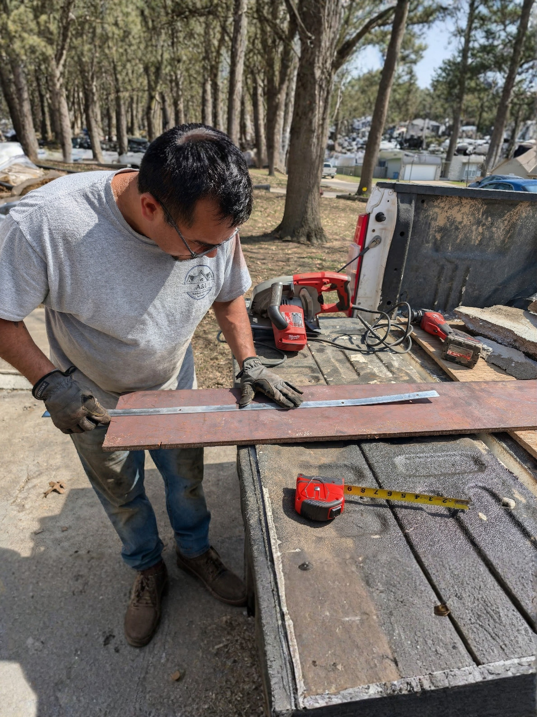 Man measuring a piece of tile or stone with a metal ruler on a worktable outdoors, with power tools and measuring tape nearby.