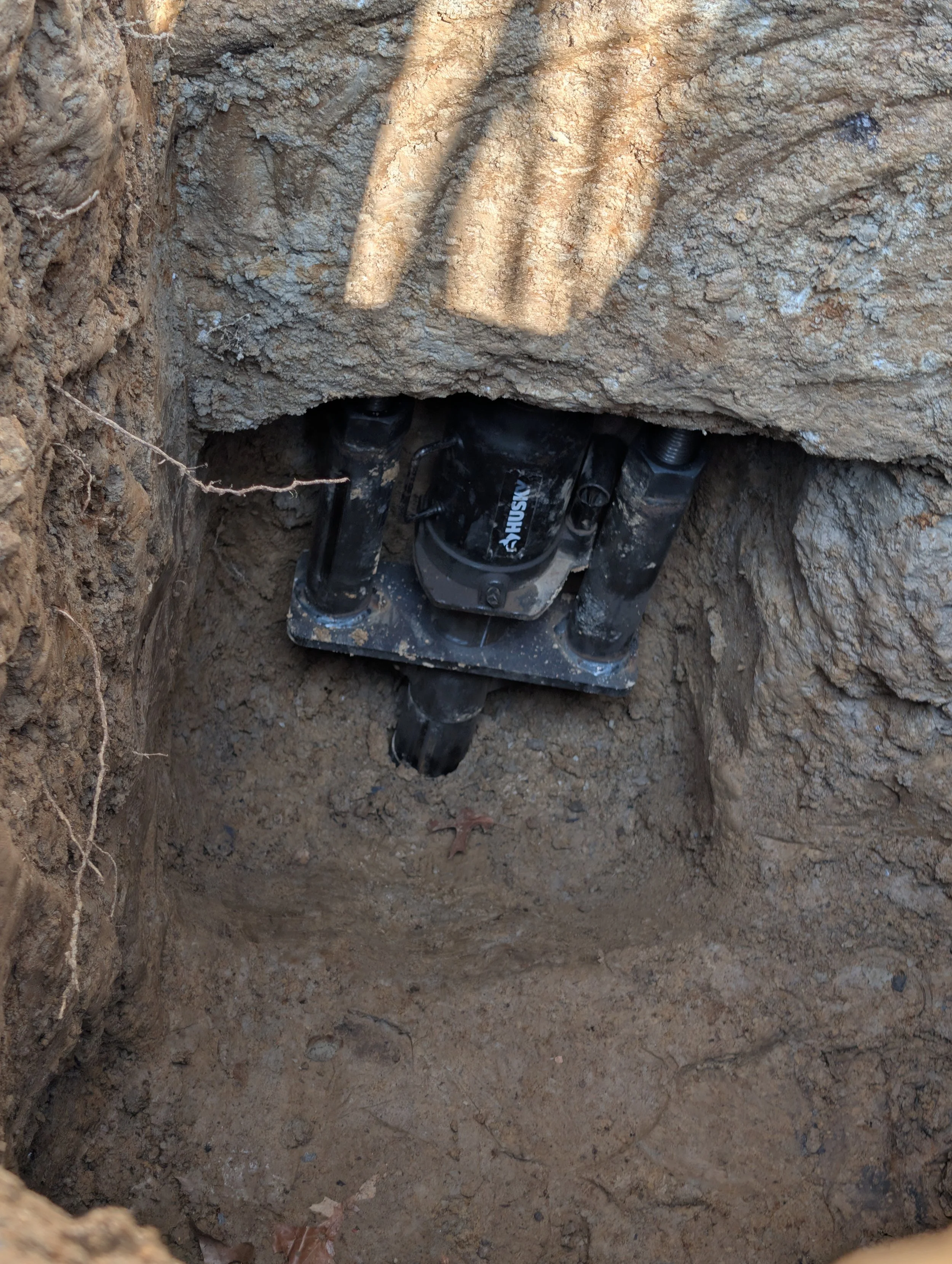 A black Husky electric motor installed in a deep rectangular hole in the ground, surrounded by dirt and soil.
