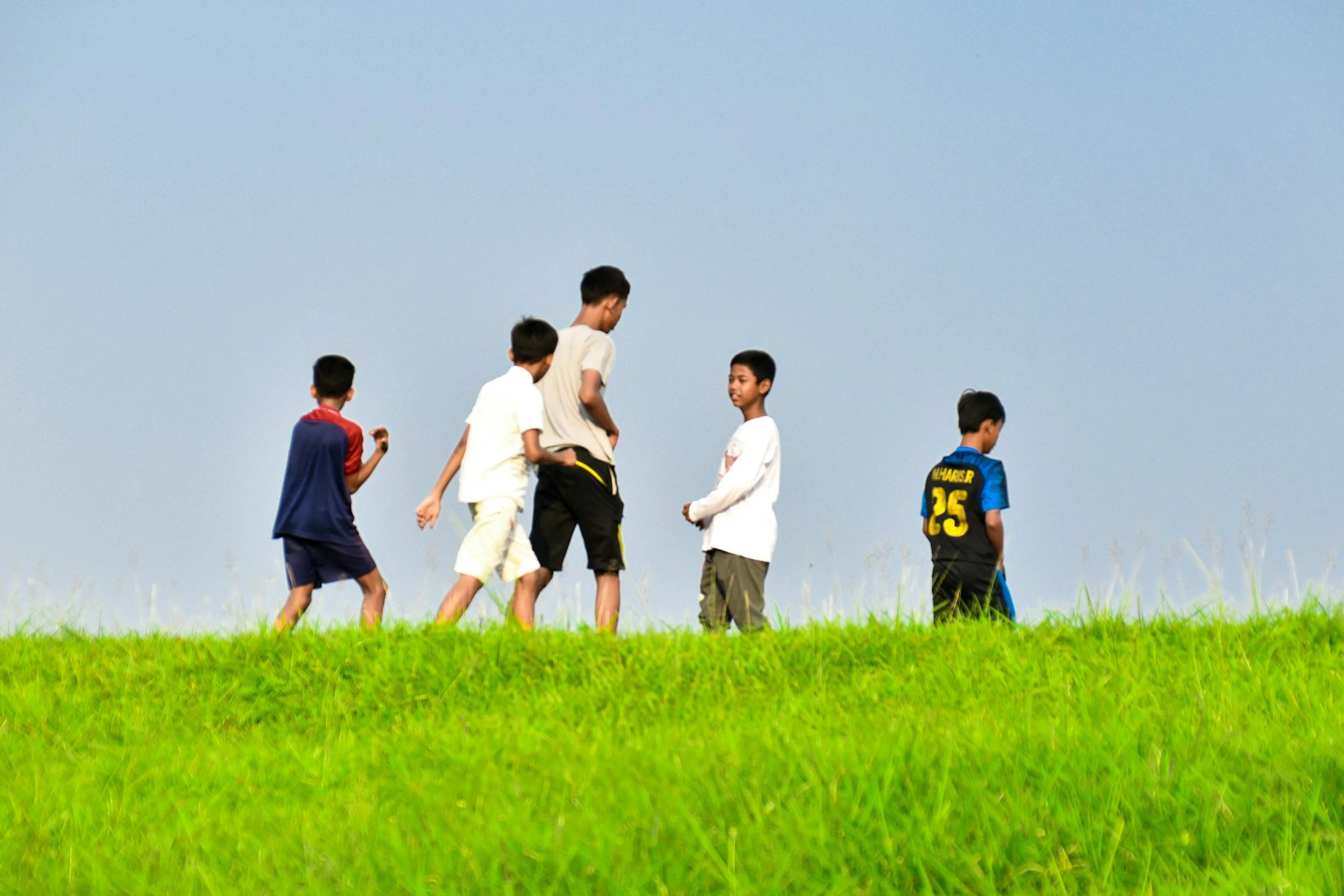 Group of boys standing on a grassy hill, under a clear sky.