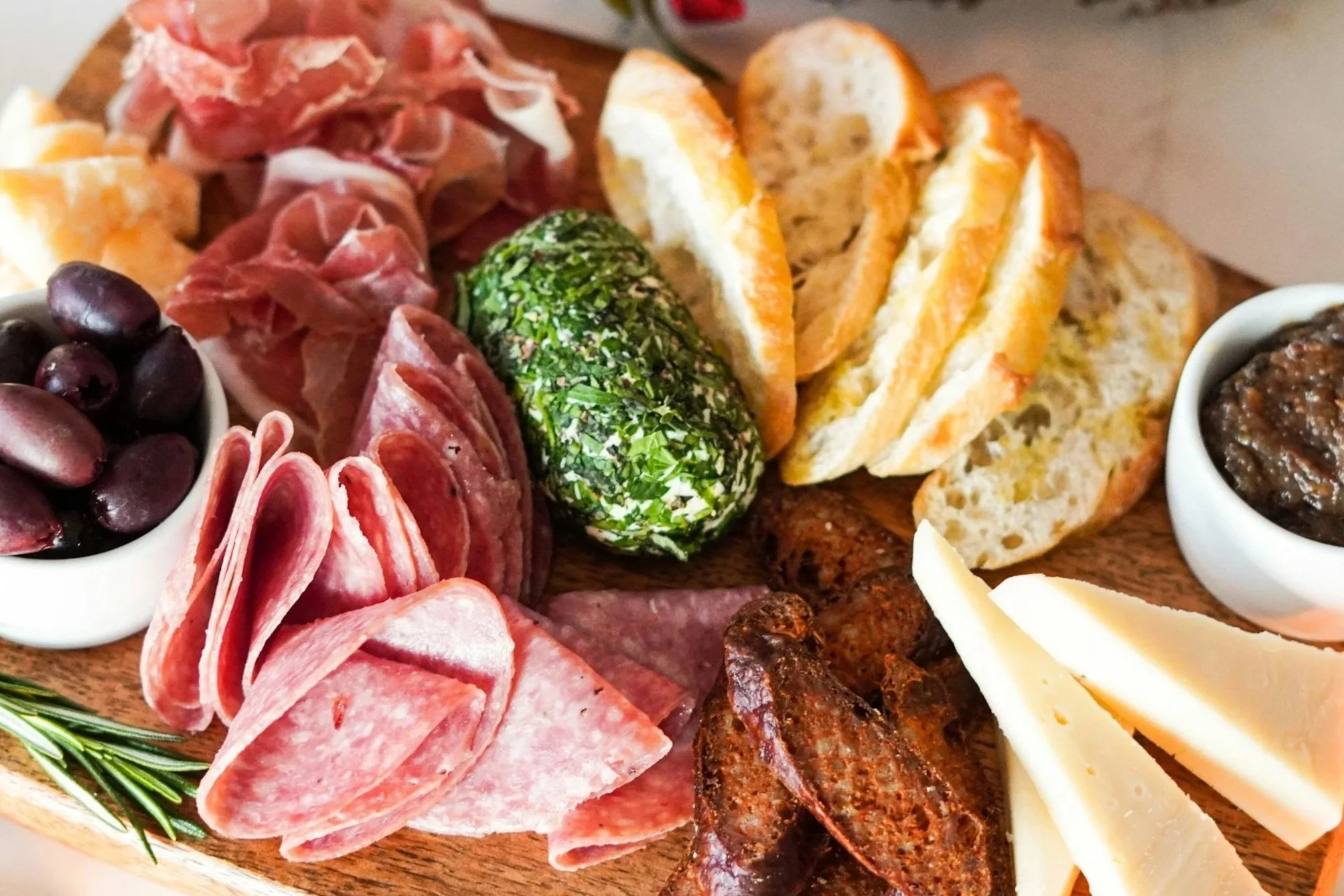 A charcuterie board with assorted meats, cheeses, bread, olives, and spreads.