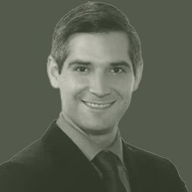 Black and white portrait of a smiling man with short dark hair, wearing a dark suit and tie