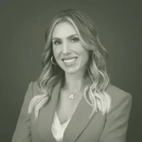 A professional woman with wavy blonde hair, wearing a blazer and smiling at the camera.