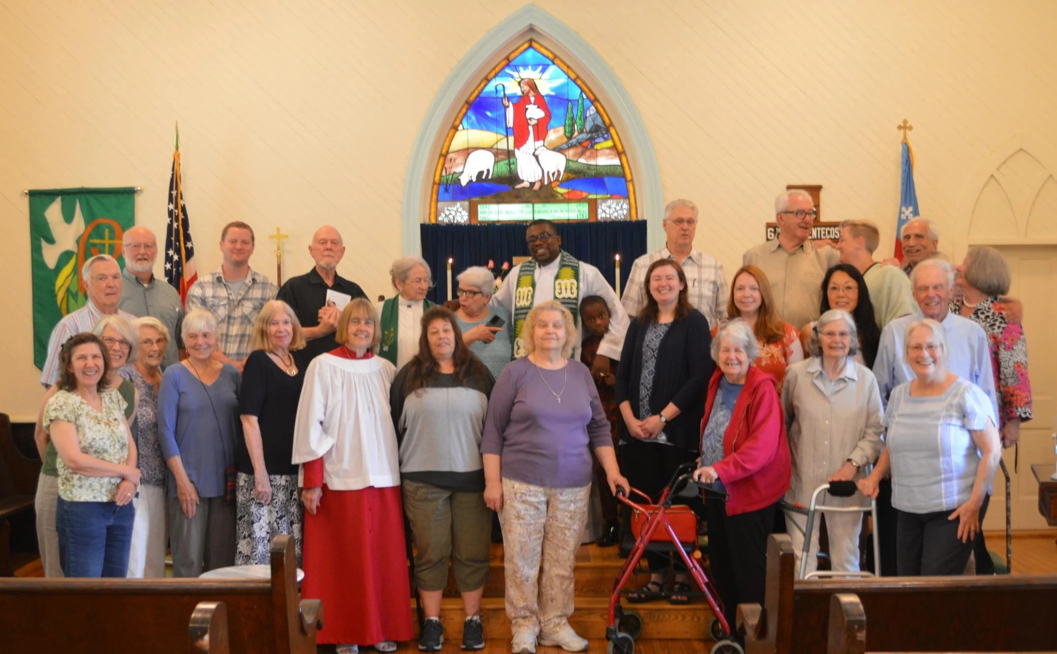 Group of church congregation members and clergy posing for a photo inside a church with stained glass window in the background.