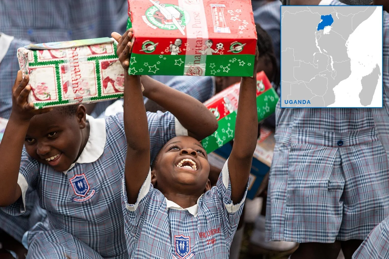 Children in school uniforms celebrating and holding Christmas gift boxes outdoors in Uganda.