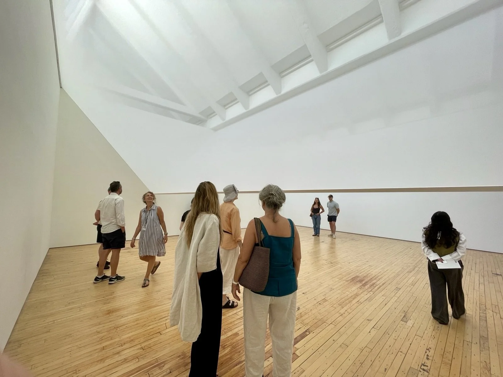 People inside a modern art gallery with wooden floors and white walls, looking at the artwork.