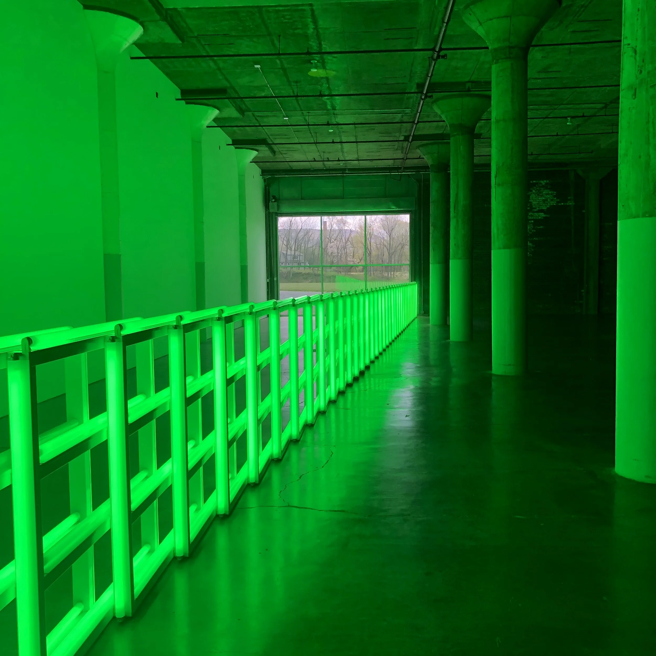 Indoor space with concrete floors, large windows, and green neon lighting along a safety railing.