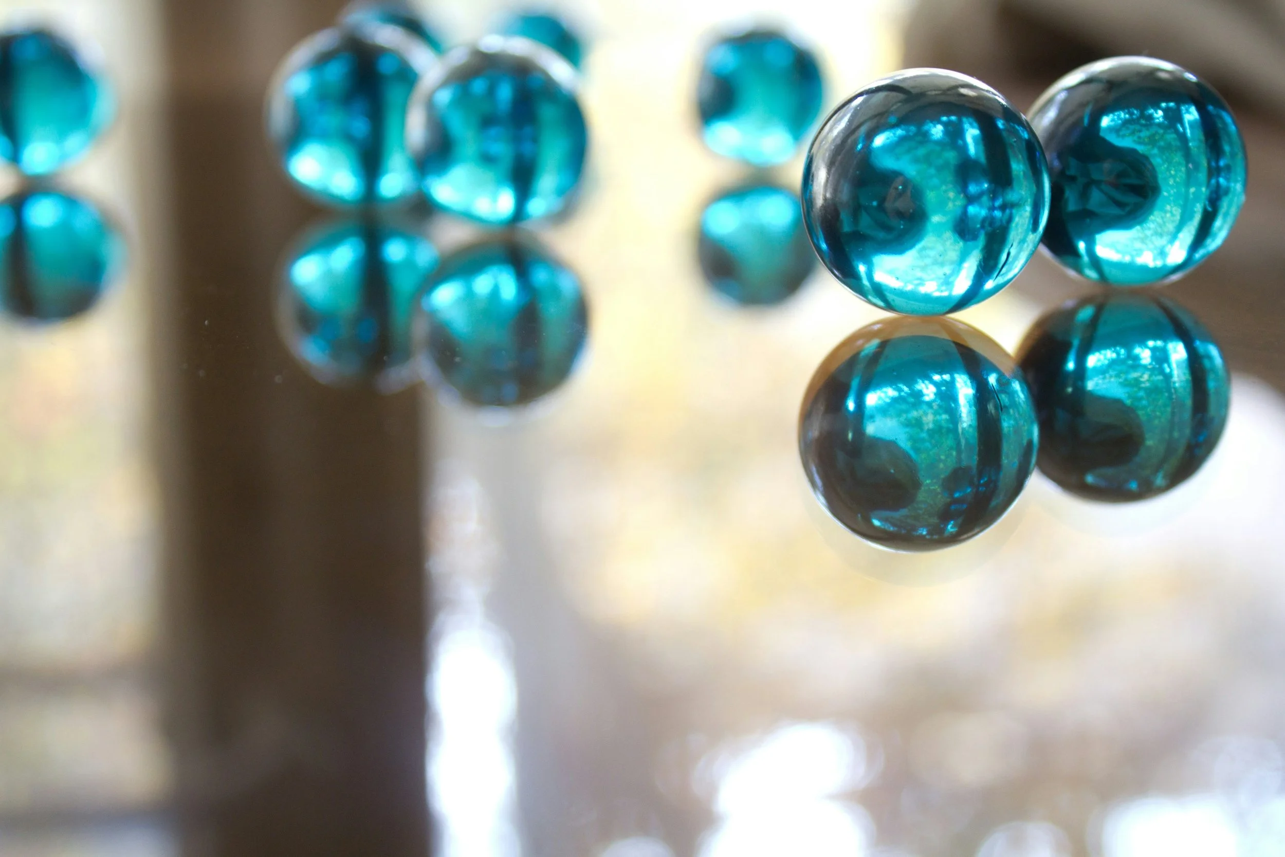 Close-up of shiny blue glass marbles on a reflective surface with reflections visible.