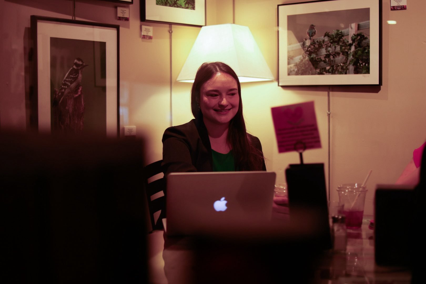 A phot oof Park smiling while sitting at at Taste Full Beans for a meetup. The background includes framed pictures on a beige wall and a standing lamp with a warm glow.