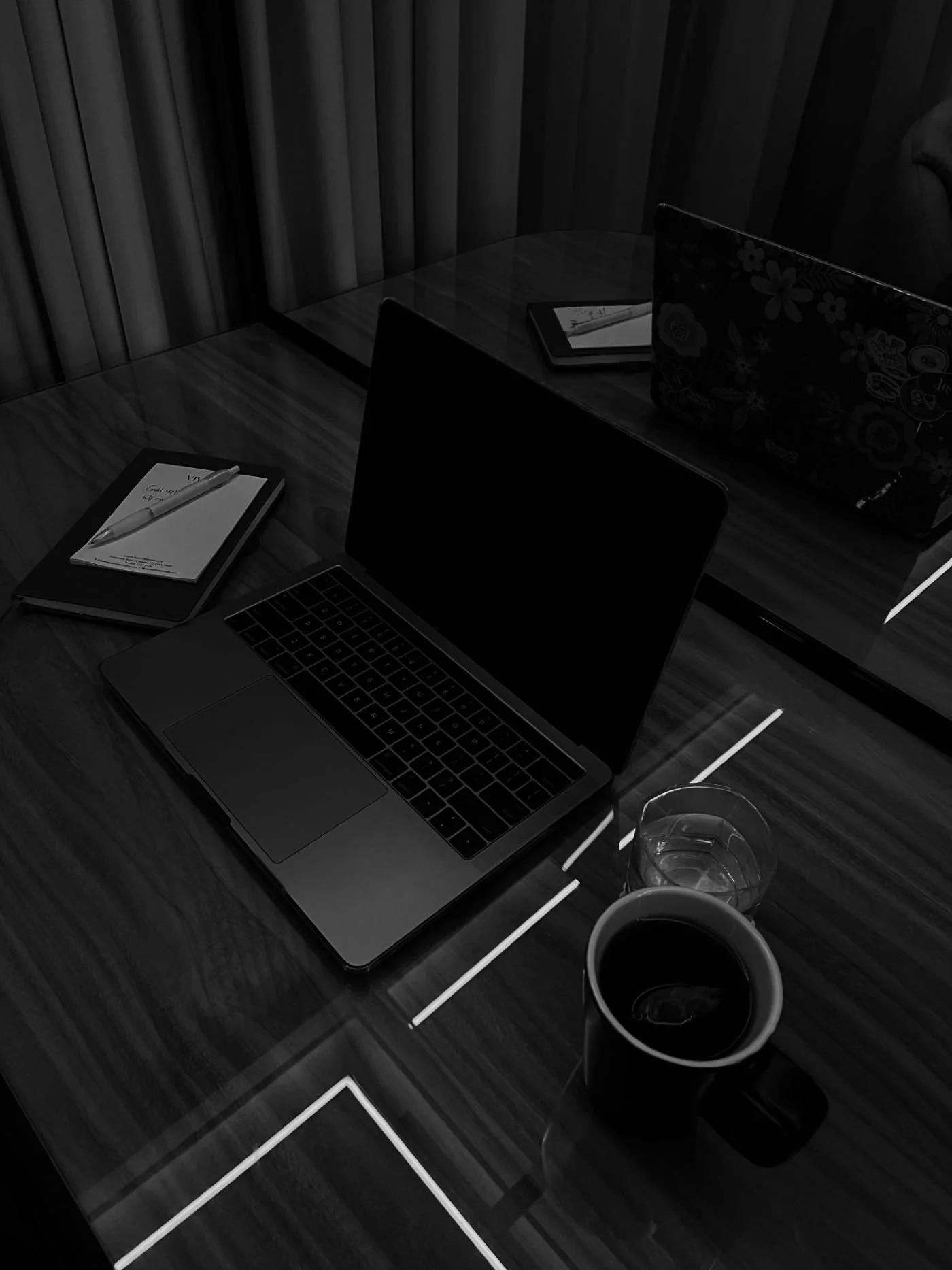 Dimly lit workspace with a closed laptop, notepads, and drinks on a wooden table.