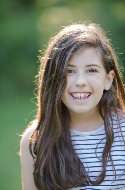 Young girl with long brown hair smiling outdoors, wearing a striped shirt