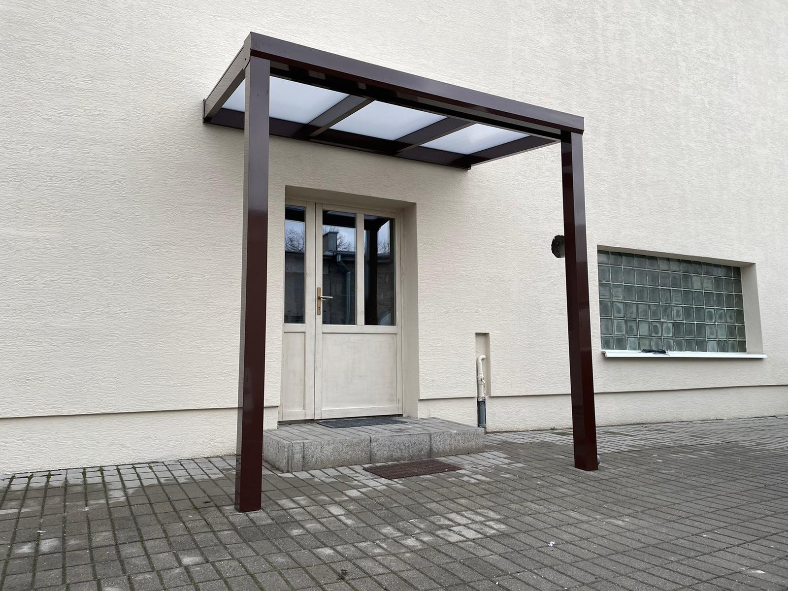 Modern, üveg- és alumíniumszerkezetű bejárati előtető fehér homlokzatú családi háznál