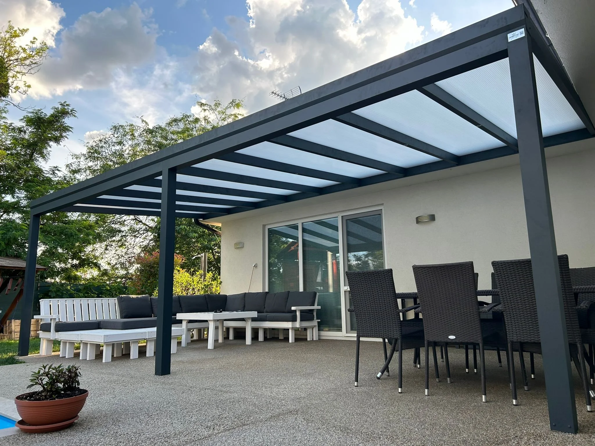 Antracit alumínium pergola modern teraszon, fehér kerti ülőgarnitúrával, étkezővel és mosott kavics burkolattal