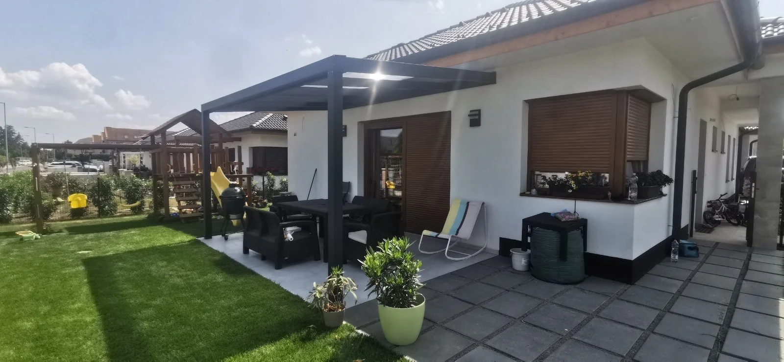 Árnyékolt étkezőrész fehér házhoz csatlakozó teraszon, pergola alatt