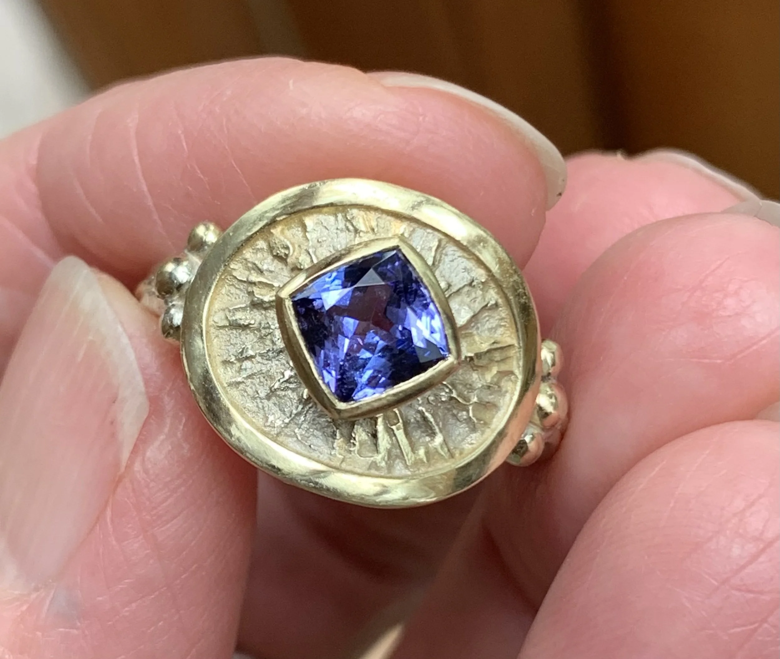 Close-up of a gold ring with a large, dark blue gemstone worn on a person's finger.