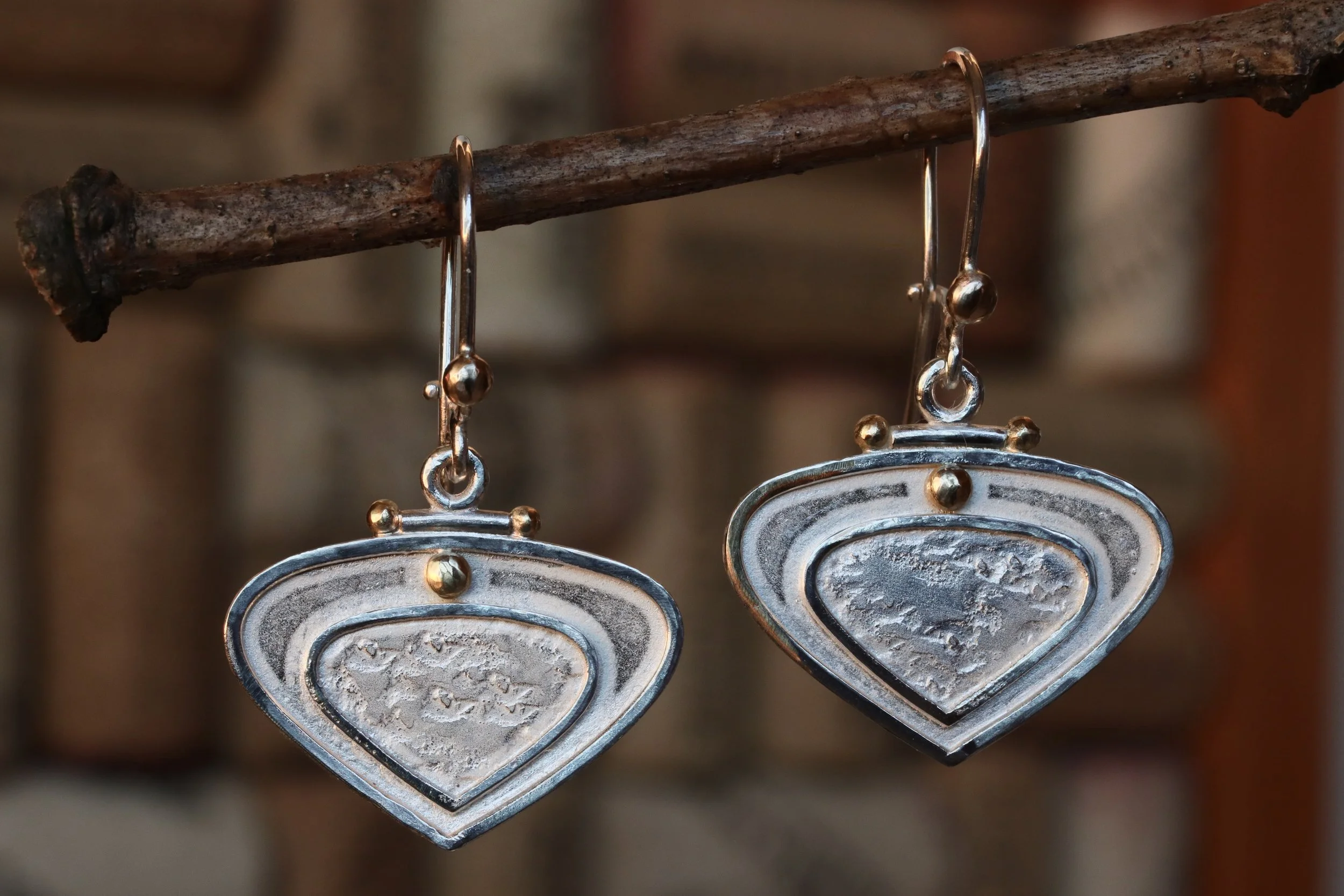 Silver heart-shaped earrings hanging from a wooden stick.