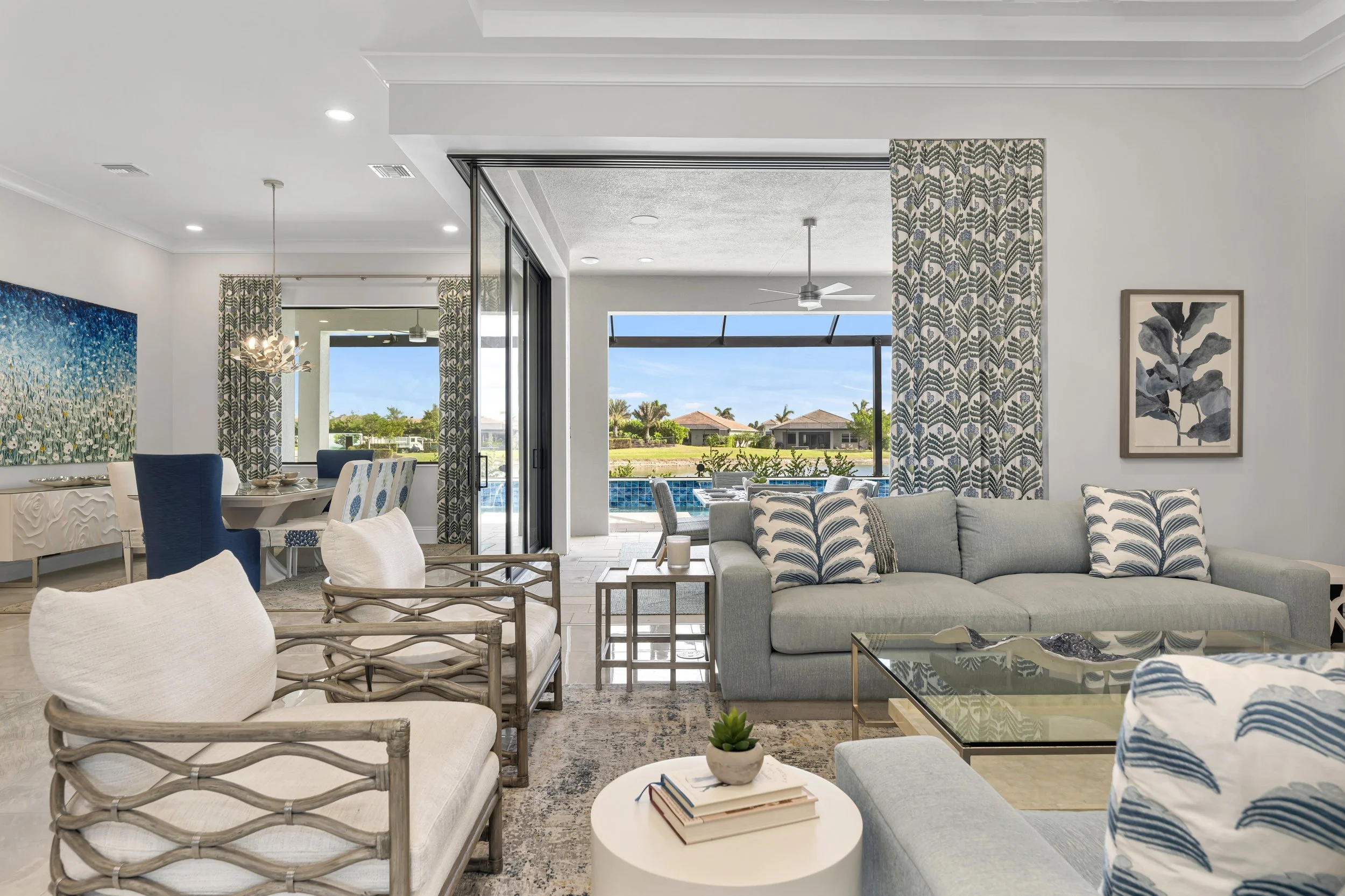 Award-winning living room design by KD Designs with a sofa and patterned pillows, a glass coffee table with decor, and a view of the outside patio with swimming pool.