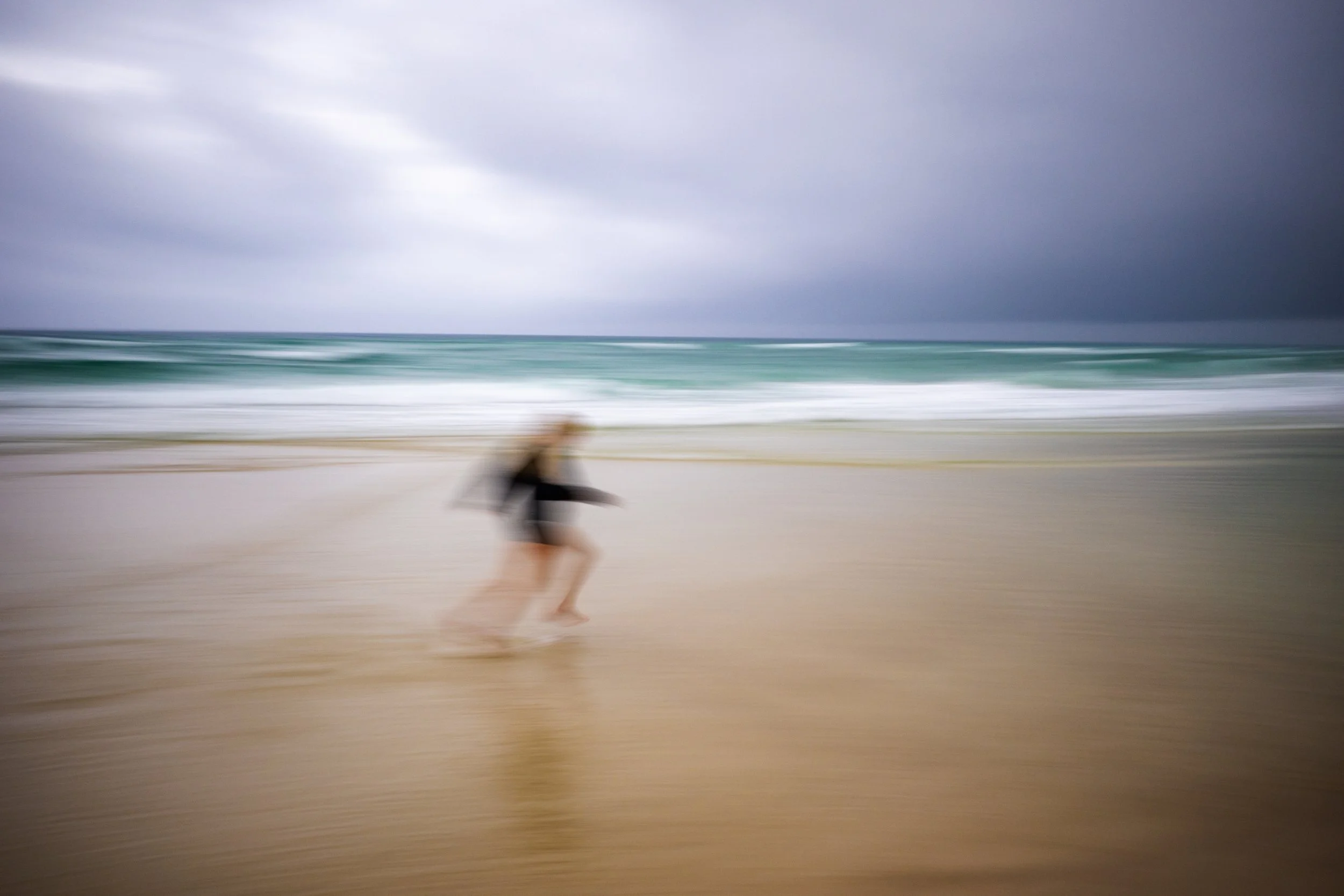 Blurry photo of a person running on a beach with stormy skies overhead, and blurred ocean waves in the background.