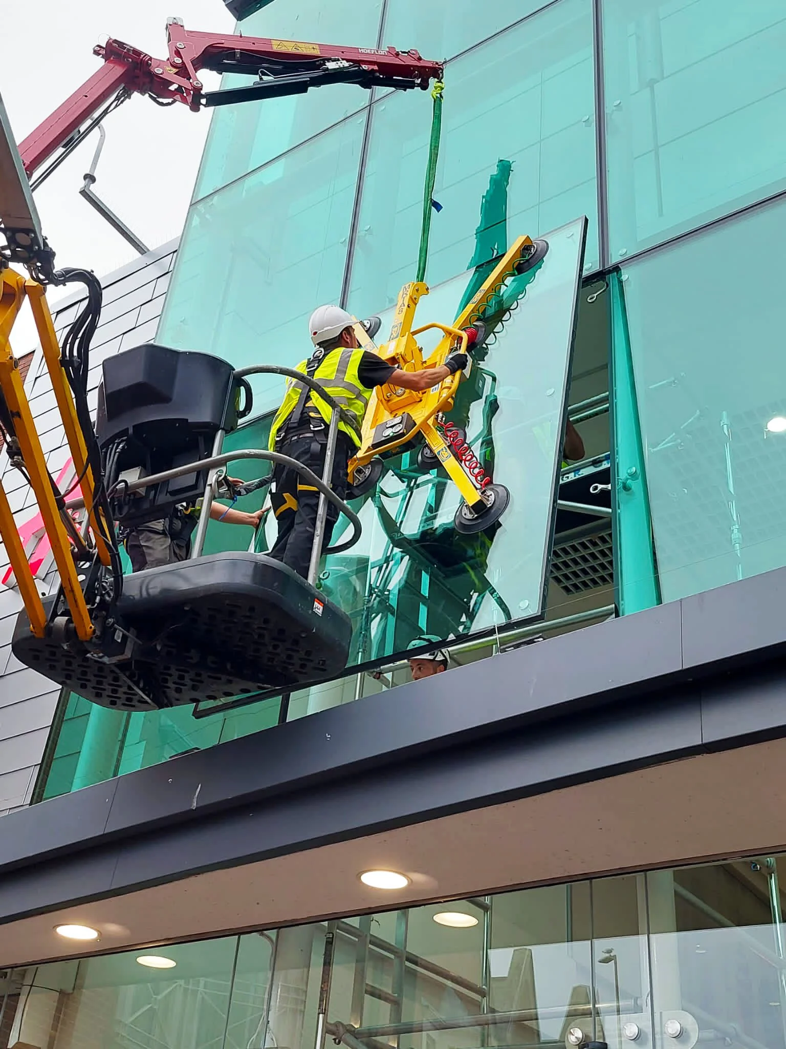 Workers cleaning the exterior glass windows of a modern building using a hydraulic lift.