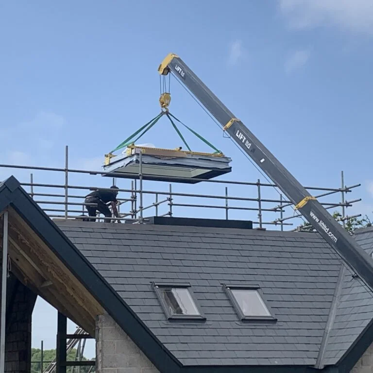 A crane holding a rooflight with a man leaning down with scaffolding all around.
