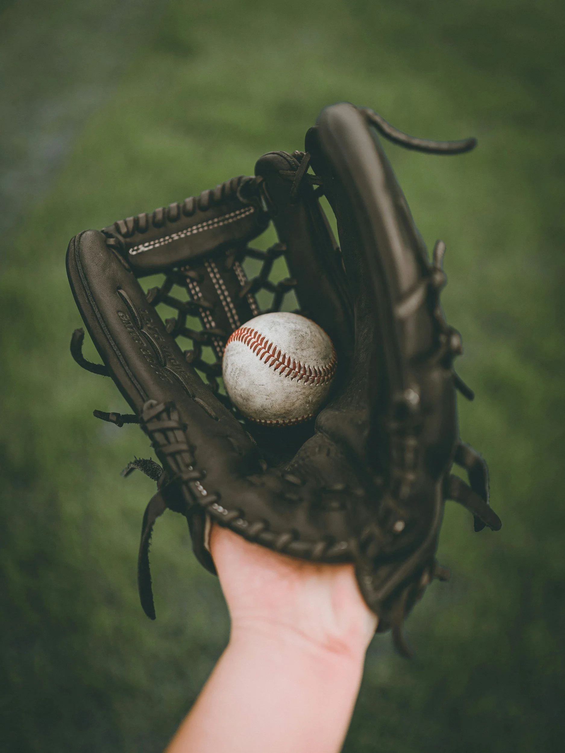 A baseball glove holding a baseball on a grassy field.