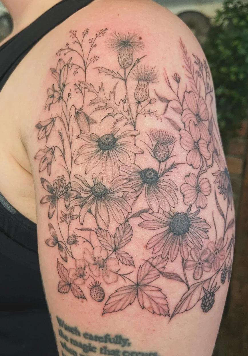 fine line tattoo of various wildflowers and berries on a person's upper arm and shoulder.