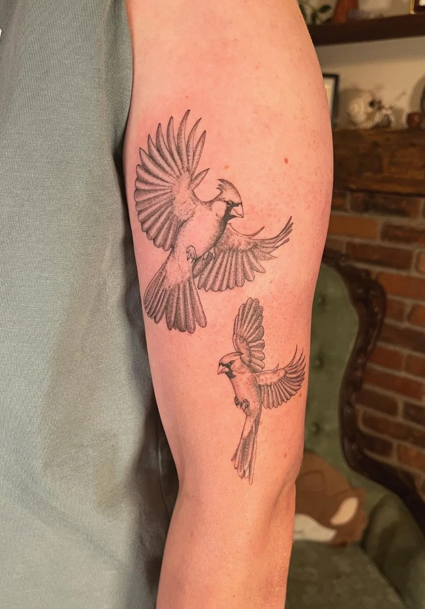 Tattoo of two birds in flight on person's upper arm, with detailed wings and feathers.