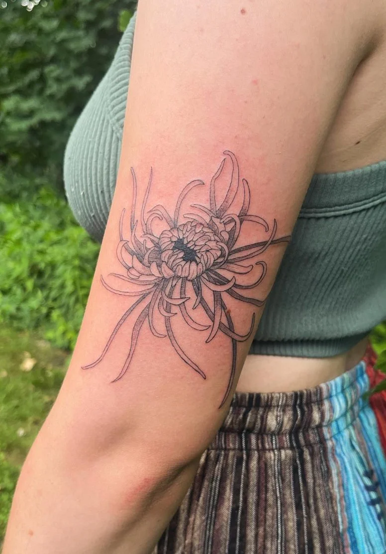 A tattoo of a flower with many long, thin, wavy petals on a person's upper arm.