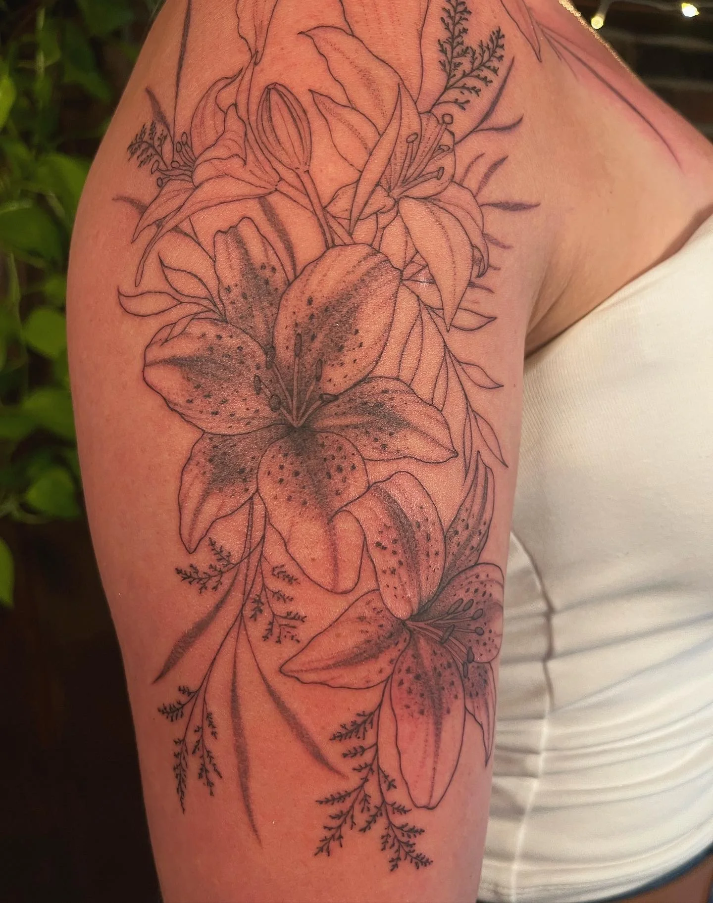 A tattoo of lilies with detailed line work and shading on a person's upper arm.