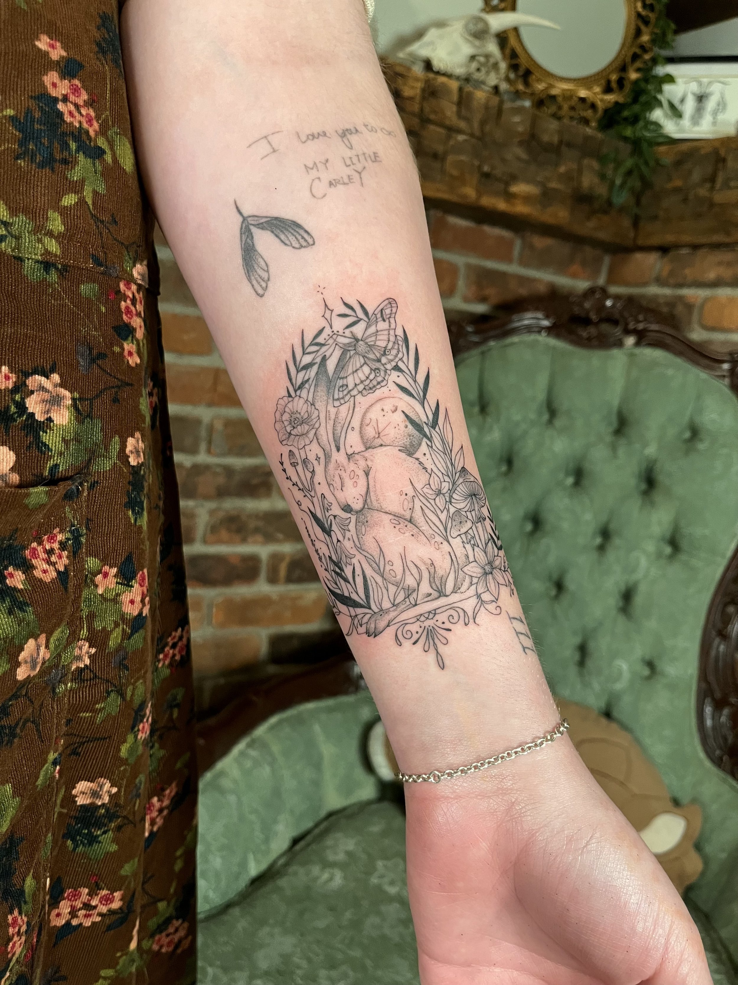 Tattoo of a vintage rabbit surrounded by leaves, flowers, and a butterfly, with a small fine line details.