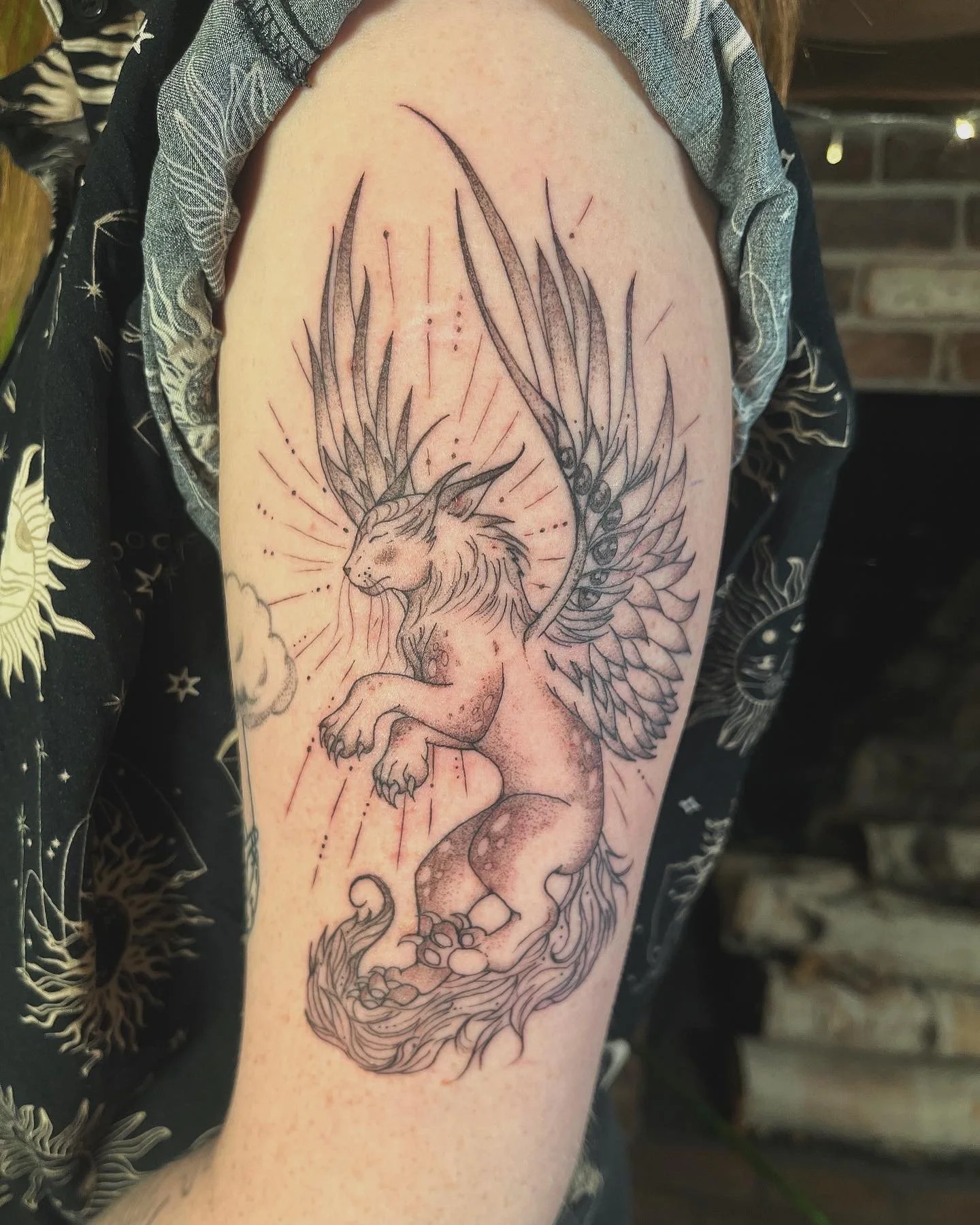 A detailed black and gray tattoo of a winged cat creature