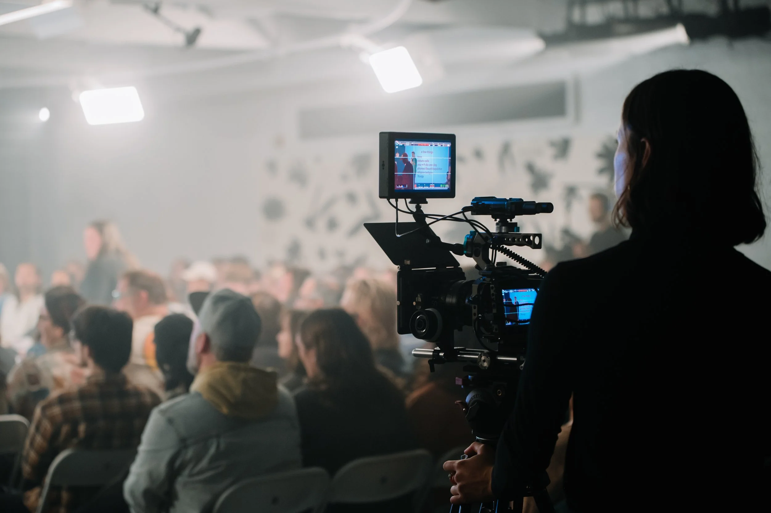 A woman filming an audience with a professional video camera at an event or conference.