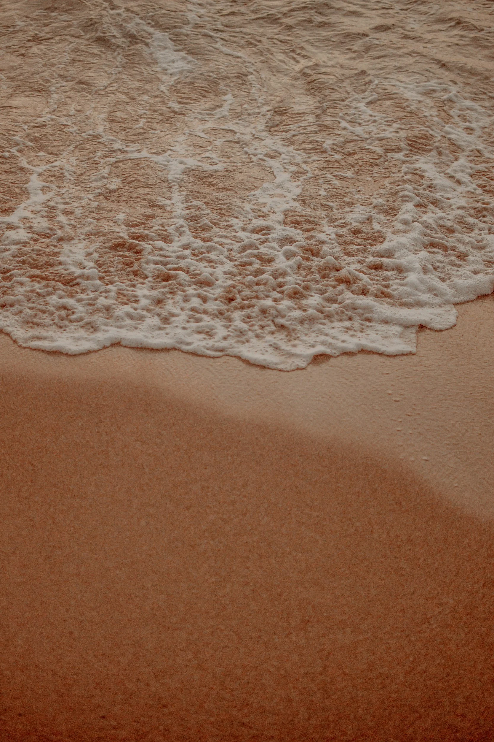 Close-up of sandy beach with gentle waves and foam washing ashore.