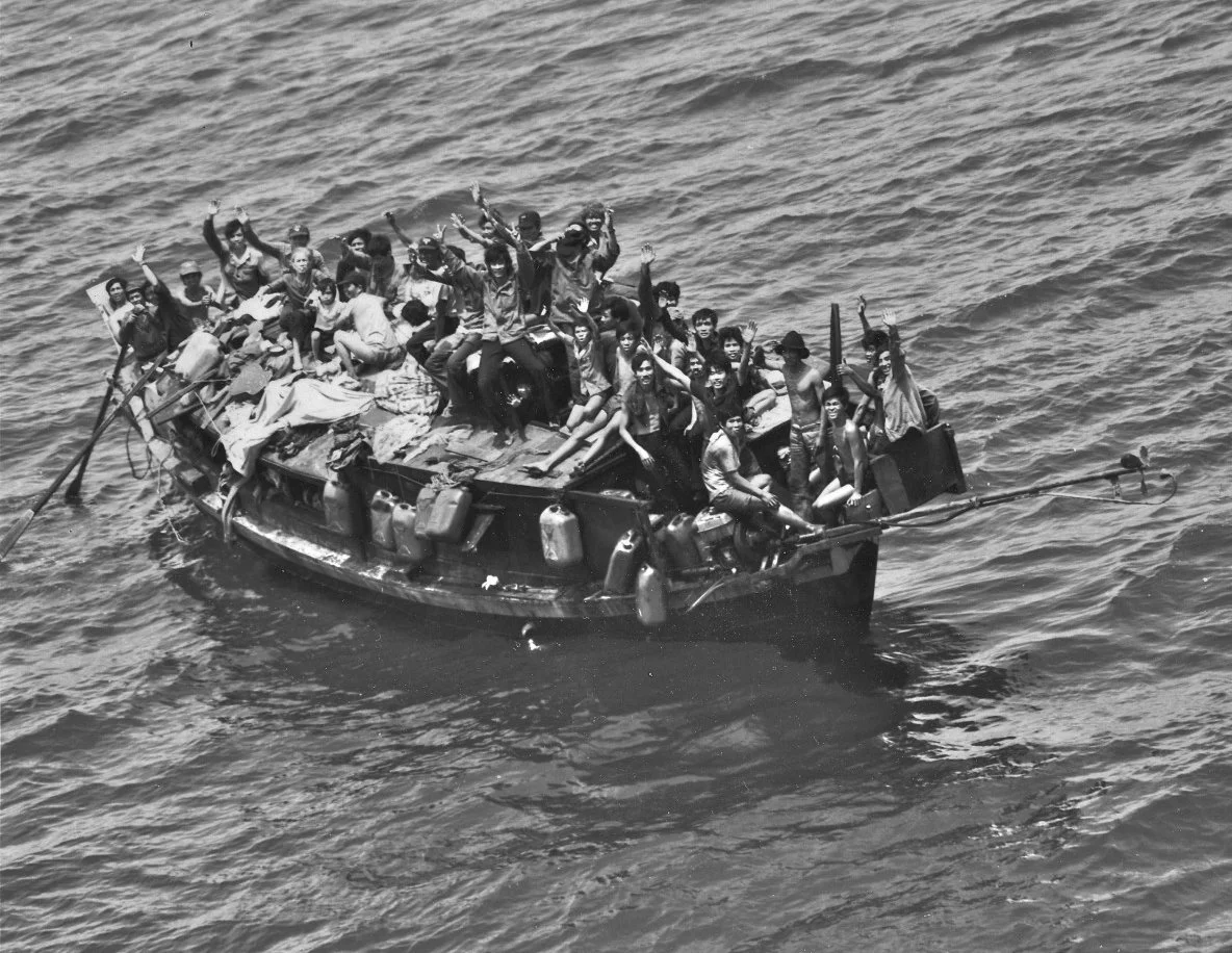 A crowded boat with many people on board, some waving, floating on the water.